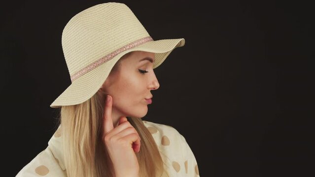 portrait profile of a young blonde woman with a hat thinking and looking down black background closeup studio shot copy space. High quality 4k footage