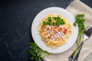Spaghetti carbonara with Crispy Bacon and Ham on white plate on black background, Carbonara pasta with parmesan cheese and cream sauce, Traditional italian cuisine.cuisine.