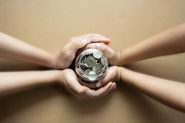 Kid hands holding coins in a jar together as saving concept for family or education.
