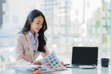 Asian businesswoman using laptop working on financial graph document using the calculator to analyze financial account in office