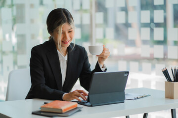 Fototapeta premium Asian businesswoman working with digital tablet, professional woman in a black business suit in office building representing a business idea.