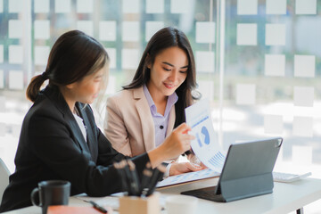 A meeting of two young Asian businesswomen to collaborate and work as a team for success in business and finance. Affiliate greetings and ideas with documents, graphs and a tablet on the table.