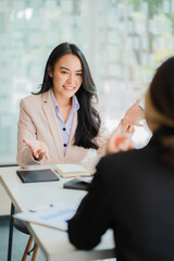 A meeting of two young Asian businesswomen to collaborate and work as a team for success in business and finance. Affiliate greetings and ideas with documents, graphs and a tablet on the table. © ArLawKa