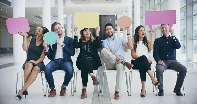 So what you thinking. 4k video footage of a group of confident young businesspeople seated next to each other while holding up speech bubbles inside of the office.