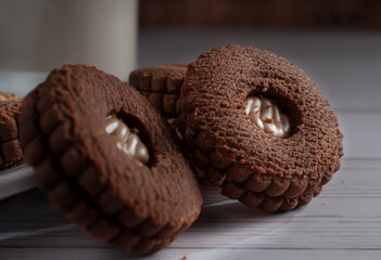 Chocolate cookie sandwich stuffed with cream chocolate on a white wooden table and a glass of ice milk in the 