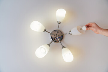 A male electrician changes the light bulbs in the ceiling light. 