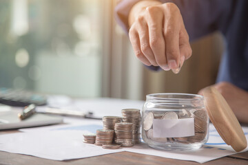 Obraz na płótnie Canvas Businessman put a coin in a piggy bank and presses a calculator for money saving planning ideas.