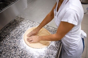 Close up view of baker hands kneading and preparing pizza dough for baking.