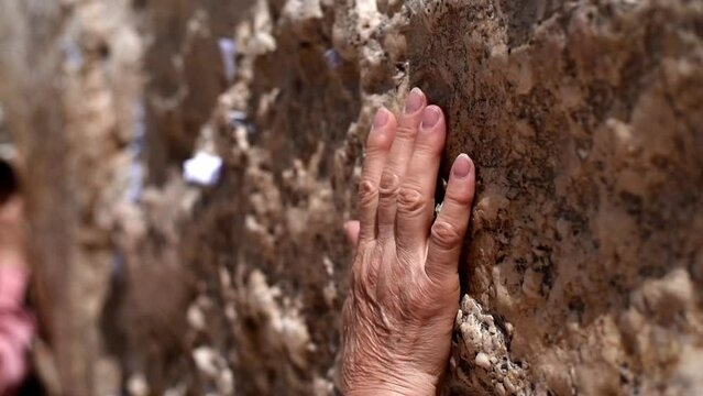 Woman's hand on Wailing Wall with notes of paper containing written prayers placing in cracks and crevices. Wall in old part of Jerusalem city. Tourism in Israel.