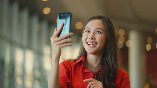 happiness asian female woman smile hand wave give a kiss to family via video call smartphone device social distancing greeting with blur mall background new normal lifestyle