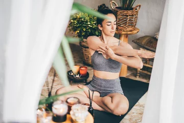 Poster Young woman sitting in the lotus position on floor in a cozy boho room. © Mariia Korneeva
