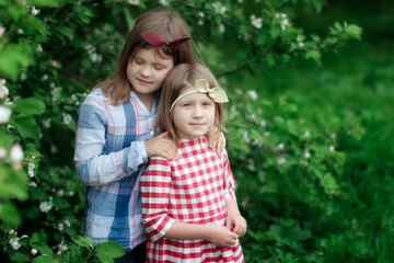 Fototapeta premium Cute sibling sister girls with a headband with a bow are hugging among green