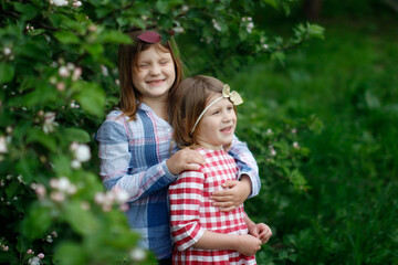 Cute sibling sister girls with a headband with a bow are hugging among green