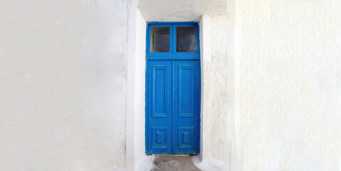 Fototapeta na wymiar Blue wooden door on empty white wall background. Greek island house front view.