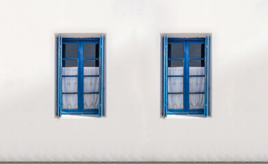 Fototapeta na wymiar Two windows with open shutters on white wall. Greek island house front view
