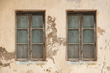 Fototapeta na wymiar Derelict home. Two window weathered aged on peeled wall. Abandoned shabby worn building exterior