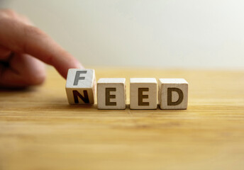 Need to feed concept. Hand flips letter on wooden cube changing the word need to feed.