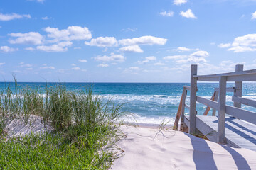 A wooden footbridge with stairs over grassy dunes descending to the inviting Atlantic Ocean on a sunny day. Florida as a luxury destination for vacation