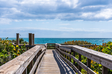 Obraz premium Wooden boardwalk leading to the beach on the Atlantic Ocean, Florida. Traditional crossing over protected sand dunes