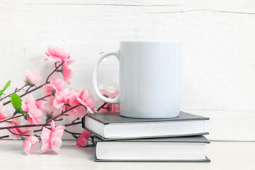 Mockup of a white ceramic mug on a table with books and flowers