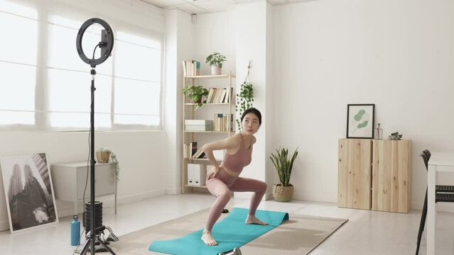 Professional female asian trainer explaining exercise while streaming an online fitness class from home. Technology, sports and healthy lifestyle.
