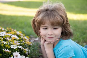 Beautiful blond little child boy with long hair smelling flower. Spring child face. Funny kids face. Happy little blond hair child with flowers. Child dreaming and smiling against spring field.