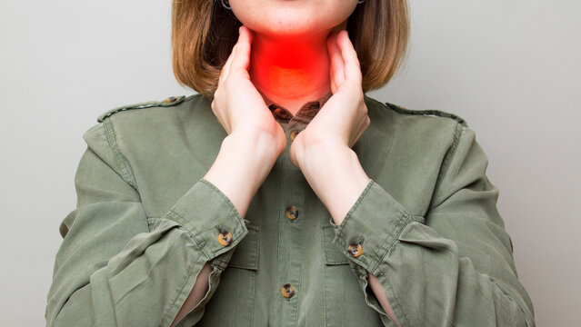 Female checking thyroid gland by herself. Close up of woman touching neck with red spot. Thyroid disorder includes goiter, hyperthyroid, hypothyroid, tumor or cancer. Health care