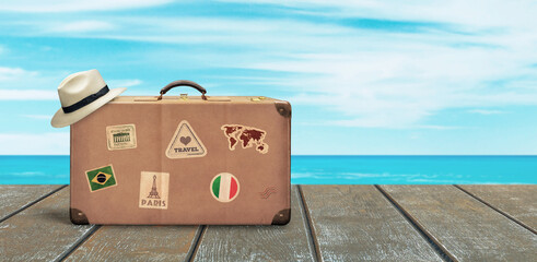 Naklejka premium Old travel suitcase and white hat on wooden floor with sea and sky in background. Copy space beside. Tropical travel concept.