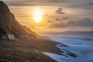 Glowing sunrise and seascape with cliffs showing colourful, different strata. 