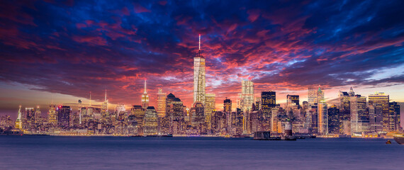 New York City Manhattan downtown skyline at dusk with skyscrapers illuminated over Hudson River panorama. Dramatic sunset sky.