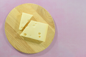 Emmental cheese bar. cut diagonally, on a round wooden cutting board. on a pink background. copy space