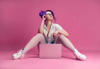 Obraz na płótnie Canvas sexy girl with glasses and purple hair with a laptop on a pink background