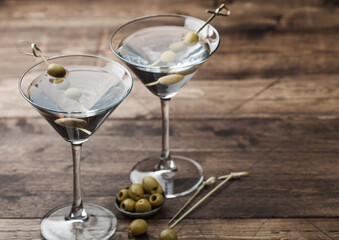 Vodka martini gin cocktail in original glasses with olives in metal bowl and bamboo sticks on wooden board.