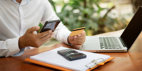 Fototapeta premium Investors use calculator are calculating investment costs and holding smartphone and laptop computer.
