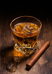 Single malt scotch whiskey in modern crystal glass with ice cubes and cuban cigar on wooden...