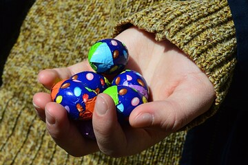 Colorful chocolate easter eggs held in left hand of teenage girl in yellow to green coloured...