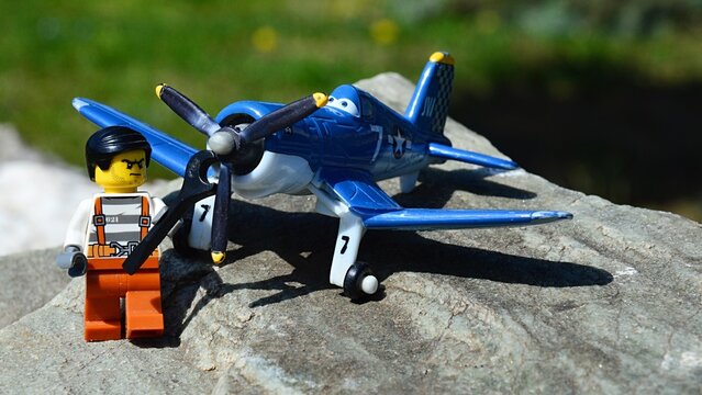 LEGO City prisoner figure with gloomy face ready to tighten the propeller of Skipper  plane model from Disney Pixar animated movie Planes, (Vought F4U Corsair WWII fighter aircraft) model on rocks.