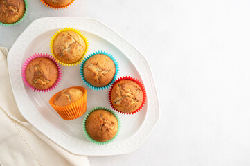 Delicious golden, homemade muffins with colorful paper cups, in a plate on a white background, copy space