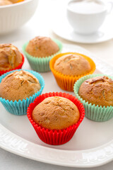 Delicious golden, homemade muffins with colorful paper cups, in a plate on a white background