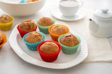 Delicious golden, homemade muffins with colorful paper cups, in a plate on a white background