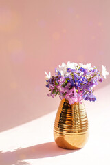 wildflowers in a golden vase on a pink background with bokeh