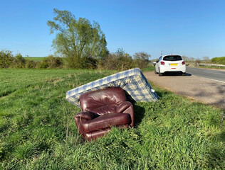 Waste furniture fly tipped on the road side, with car in background. Landscape view.