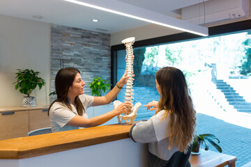 Physiotherapist holding a model of spine and showing and explaining the spinal hernia to patient
