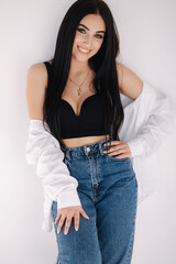 Pretty woman barefoot in studio. Beautiful brunette girl in black topic with white shirt and blue denim jeans. White background of cyclorama