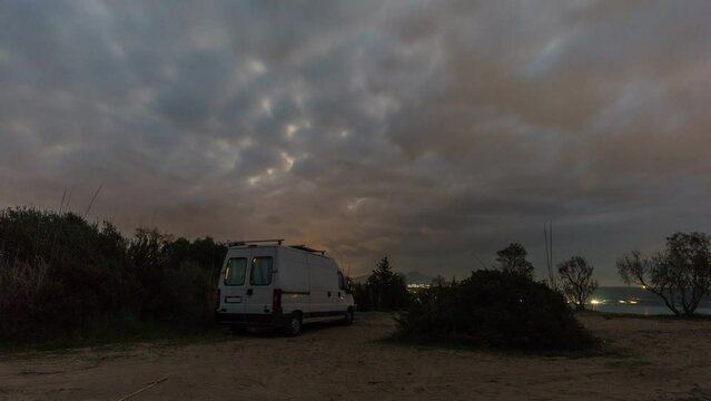 Time lapse of a camper van on the beach with rising moon and moving clouds during evening twilight, Peloponnese, Greece
