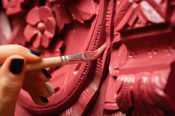 Closeup of carved ornaments on charming wooden cupboard and female hand painting it in red color...