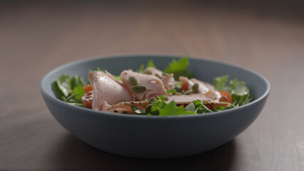 making salad, pumpkin seeds fall over turkey on frisee lettuce in blue bowl on wood table