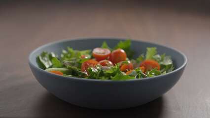 making salad, cherry tomatoes fall over frisee lettuce in blue bowl on wood table