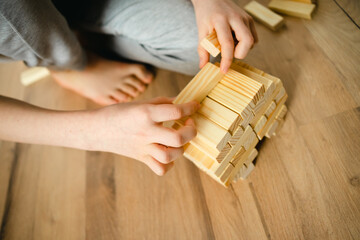 close-up. person stacks wooden blocks of the designer on the floor. children's hands. Board Games. entertainment in the bomb shelter - obrazy, fototapety, plakaty