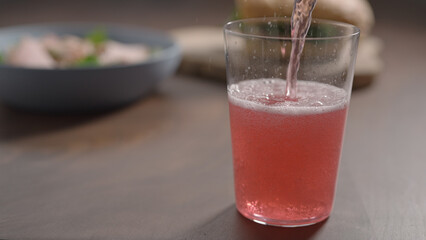 pour pink drink in tumbler glass on wood table